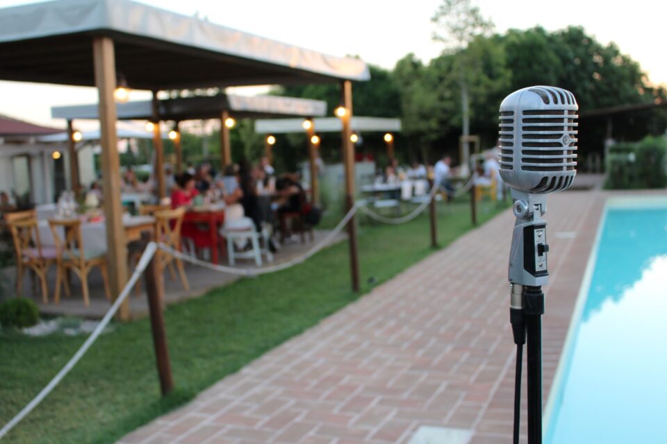Microfono davanti alla piscina della Favorita con pubblico seduto per evento musicale estivo a Bastia Umbra