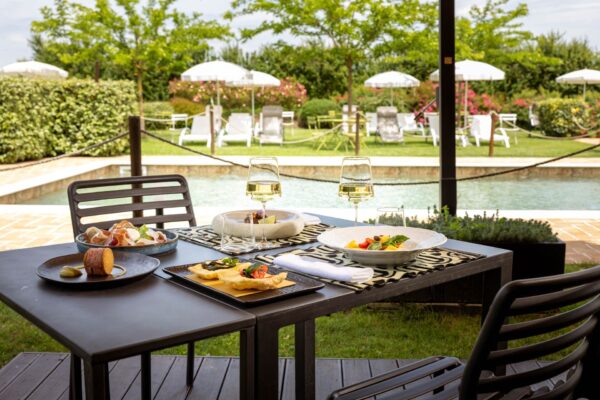 Piatti estivi e calici di vino serviti a bordo piscina all’Osteria Favorita a Ferragosto 2025